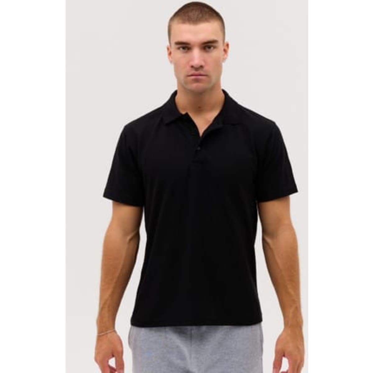 A black polo shirt displayed on a model, featuring a collar and a logo, with short sleeves.