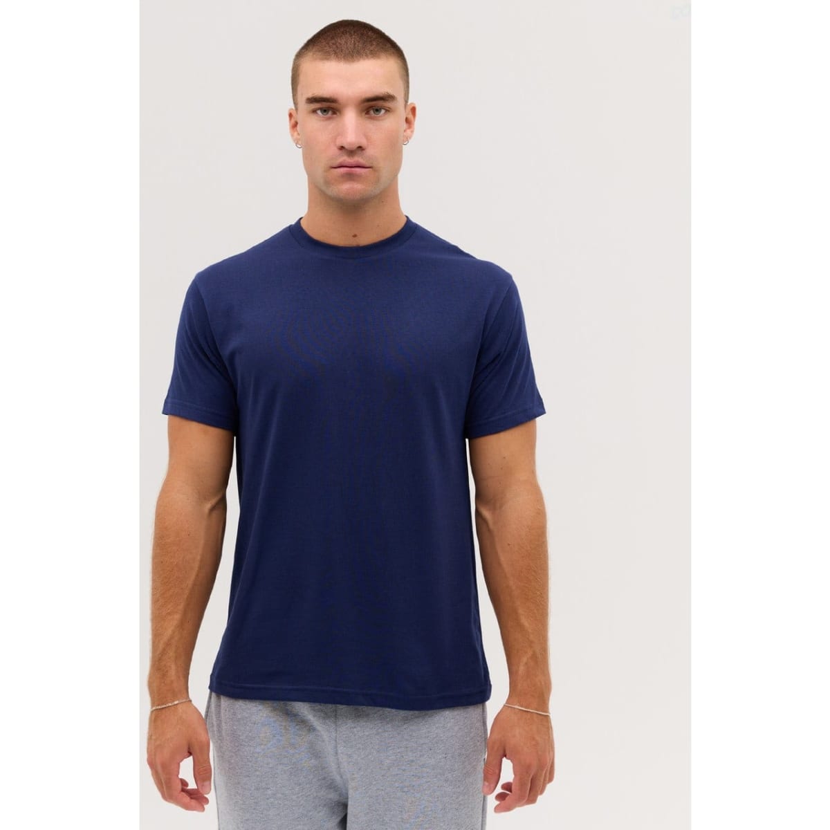 A navy T-shirt displayed on a model, featuring a simple design and short sleeves. The model has short hair and a neutral expression.