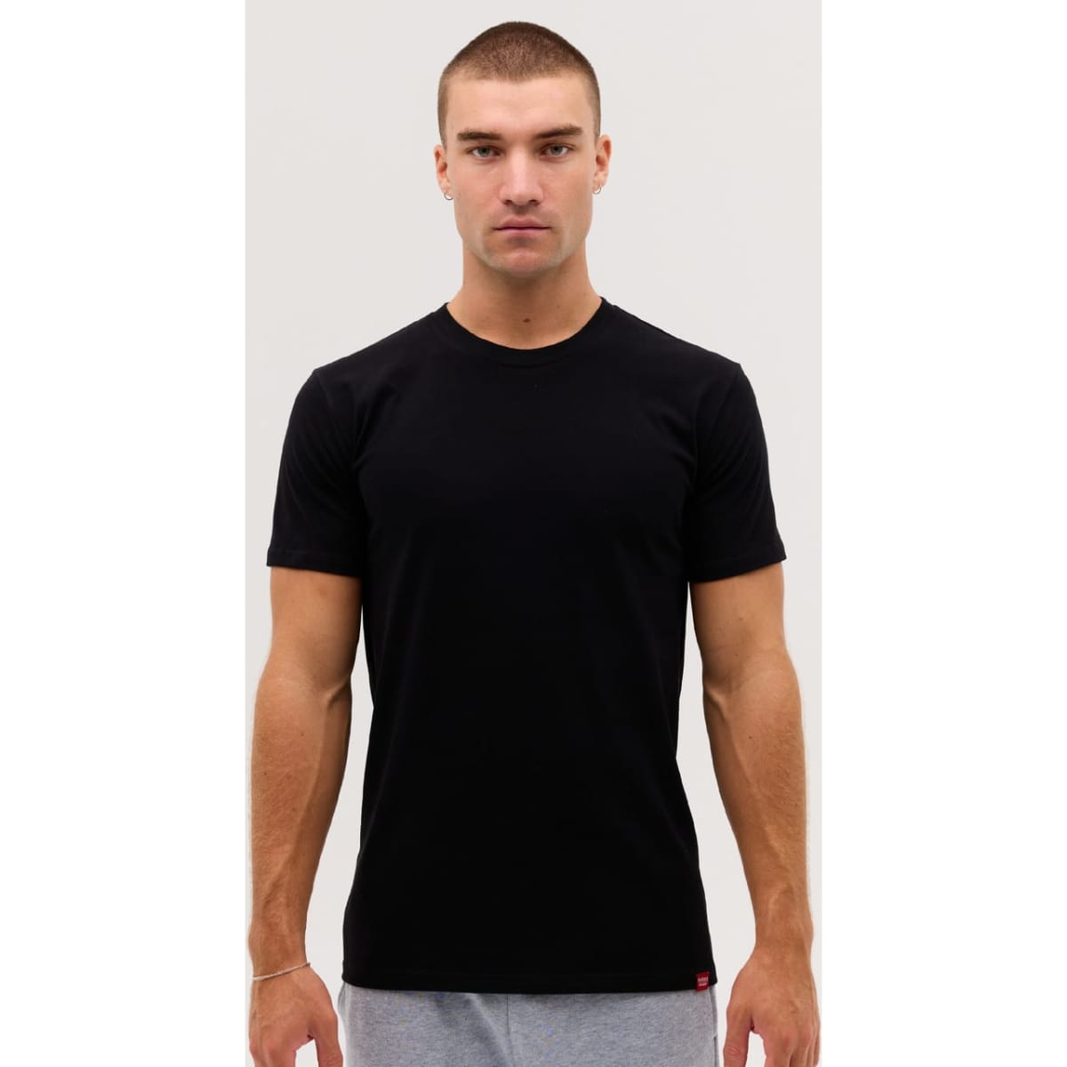 A black short-sleeved T-shirt displayed on a model, featuring a subtle logo at the hem.