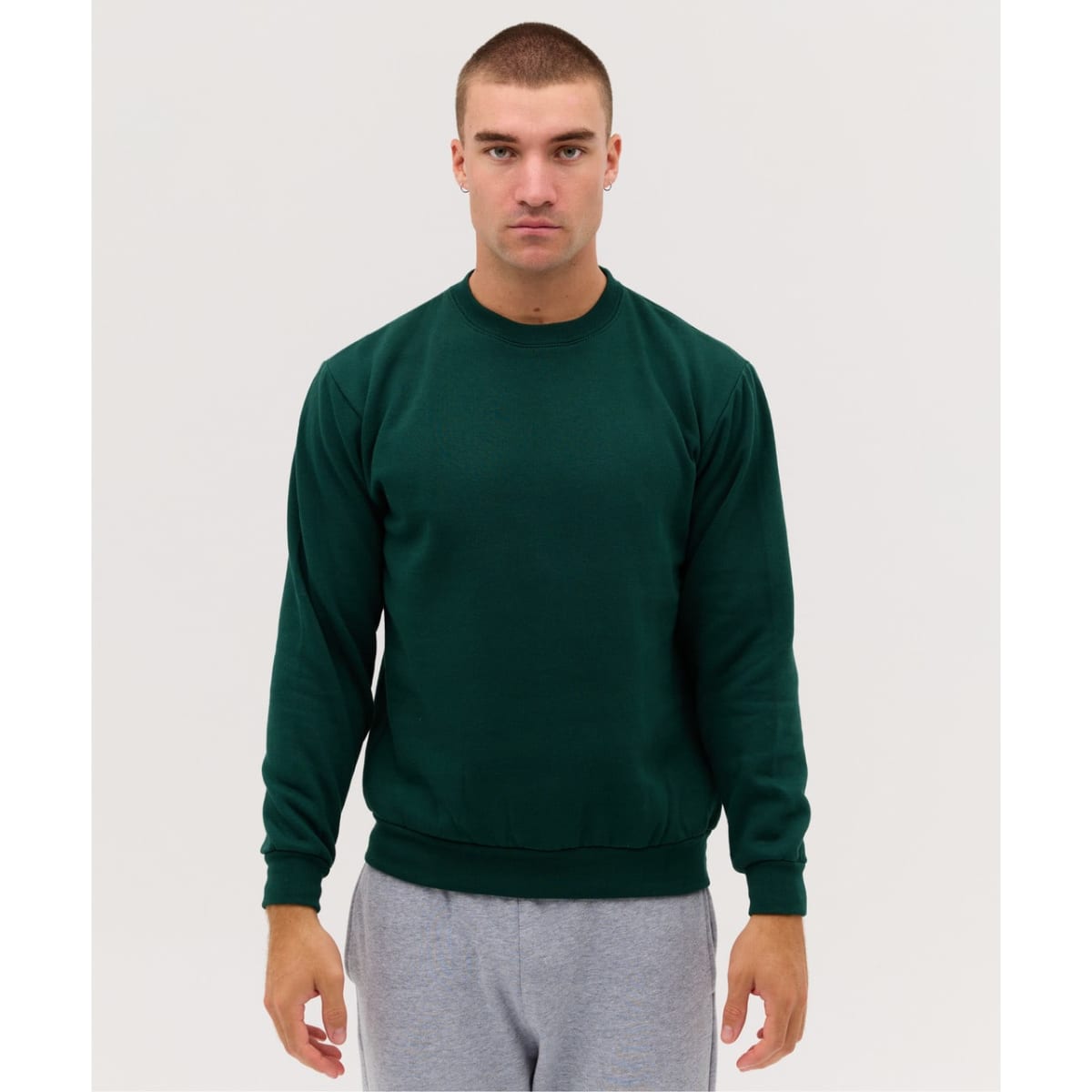 A green crew jumper displayed on a model, featuring long sleeves and a simple design. The model wears grey pants.