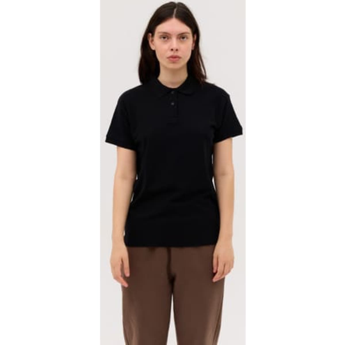 A woman wearing a black polo shirt with a collar, featuring a logo, paired with brown trousers.