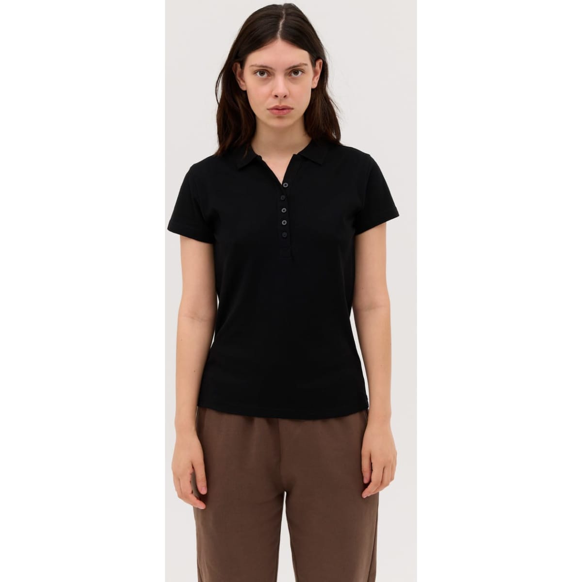 A black women's polo shirt with a collared neckline and button details, displayed on a model.