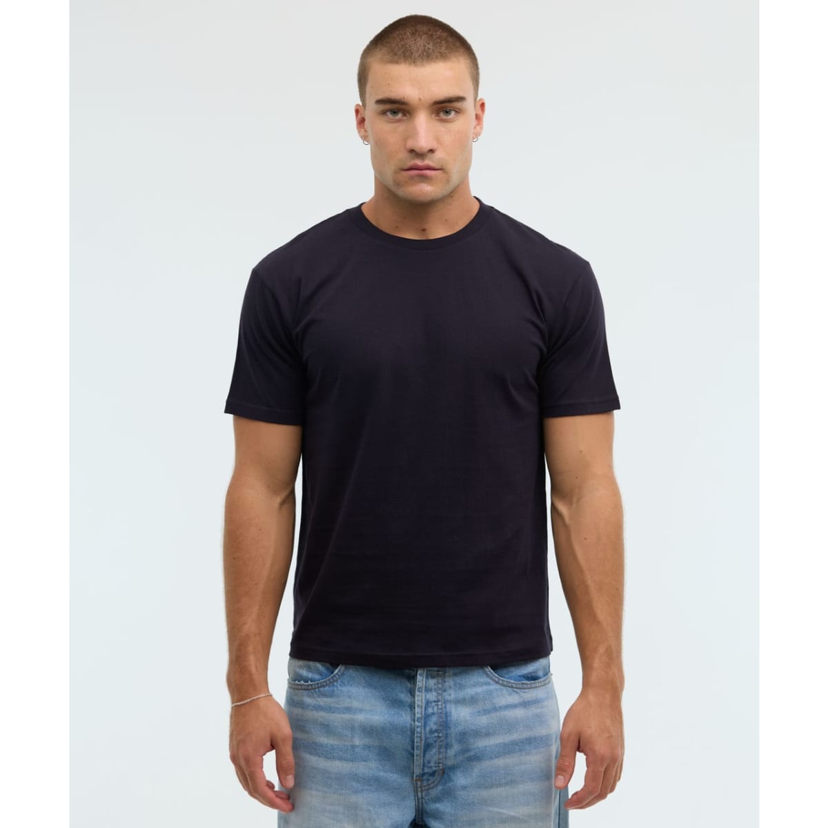 A dark navy essential tee displayed on a male model, paired with light blue denim jeans, featuring a simple design.