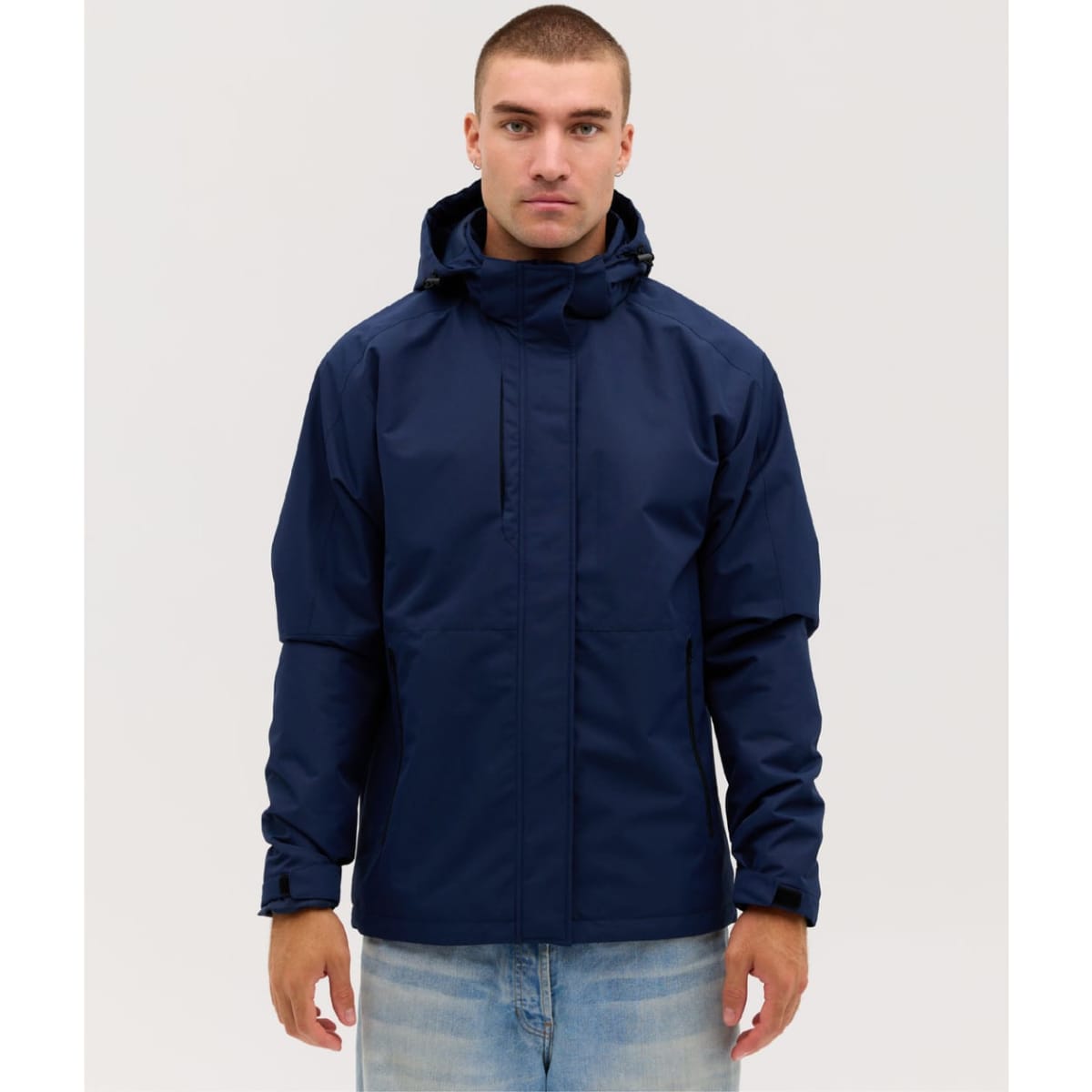 A navy blue soft shell jacket with a hood, features a front zip and a logo. Styled on a model against a neutral background.