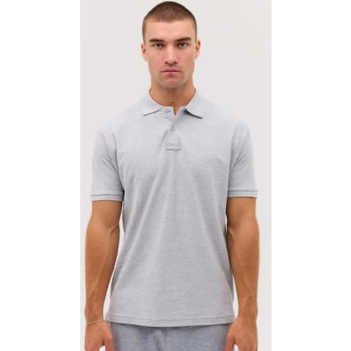 A grey polo shirt displayed on a model, featuring a collar and short sleeves. It has a logo on the chest.