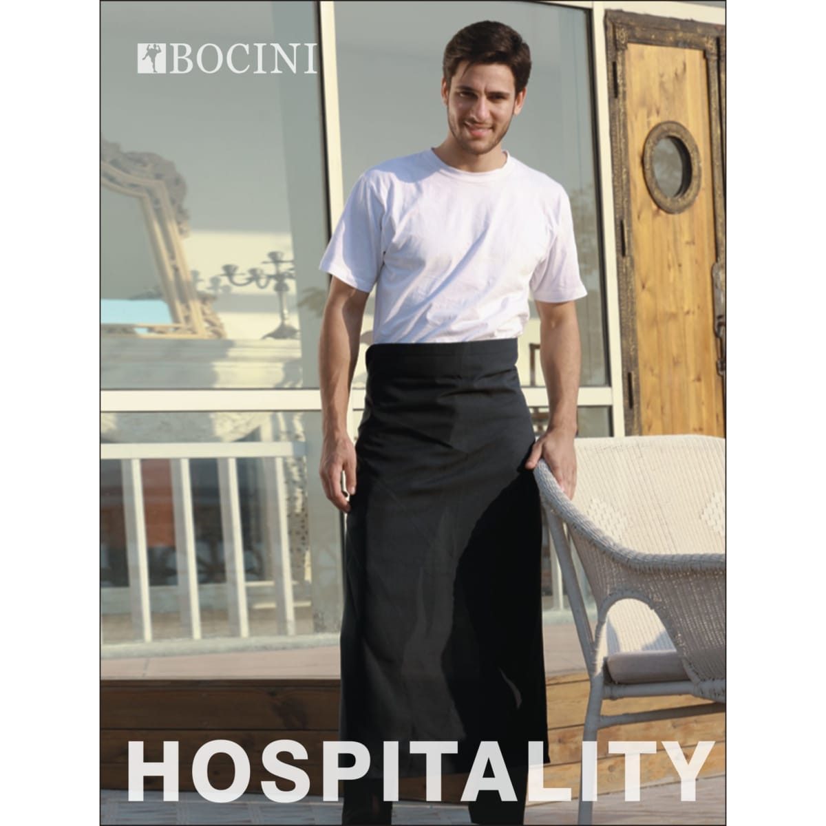 A man wearing a black cotton drill continental apron without pockets stands outdoors, featuring a logo on the apron.