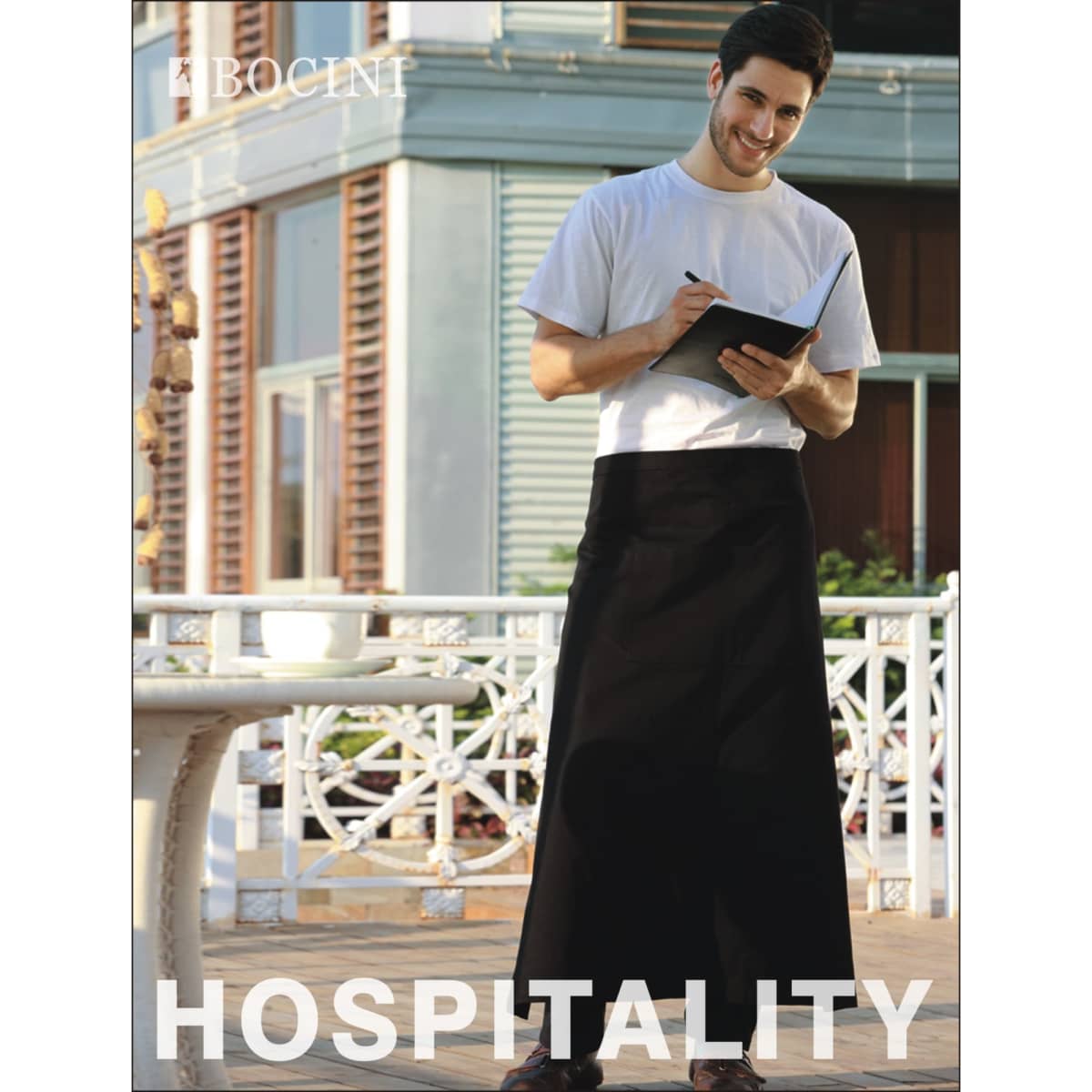 A man in a white T-shirt and black polyester drill apron stands, holding a notepad. The apron has no pockets.