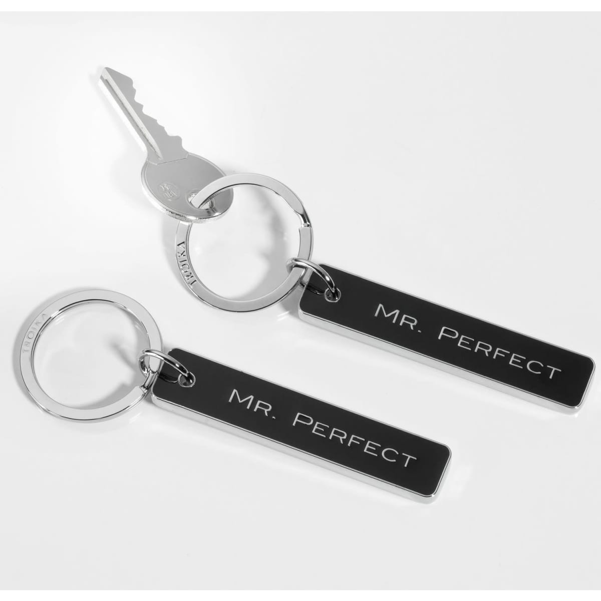 A keychain with two black metal tags featuring the inscription "MR. PERFECT," attached to a key.