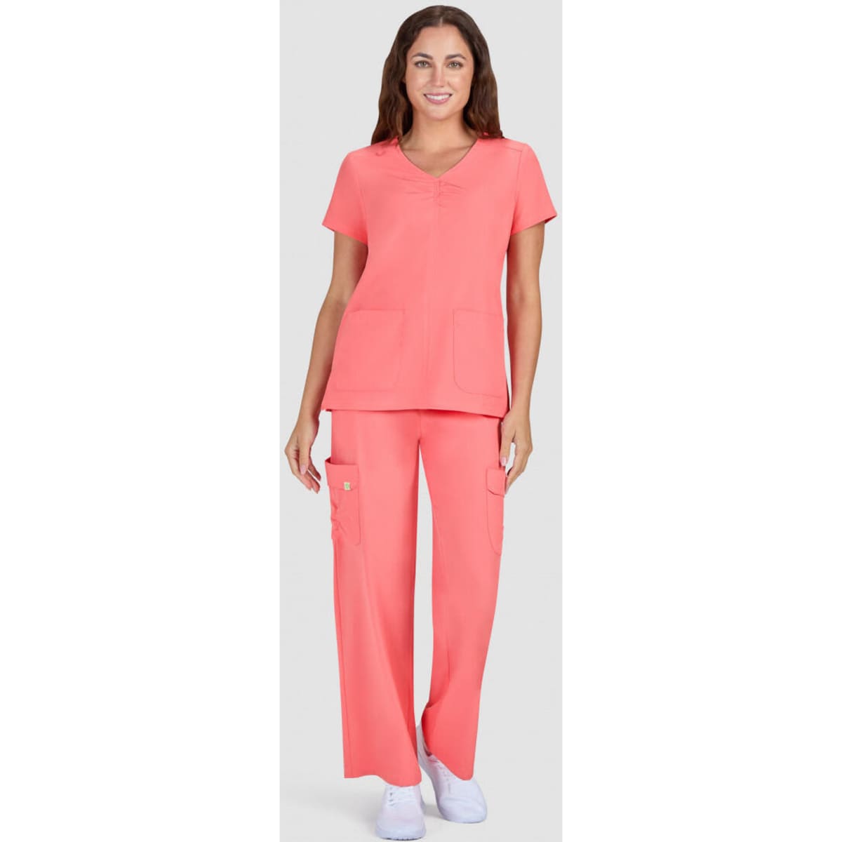 A pair of coral scrubs featuring a short-sleeve top and long pants, with pockets, worn by a model.