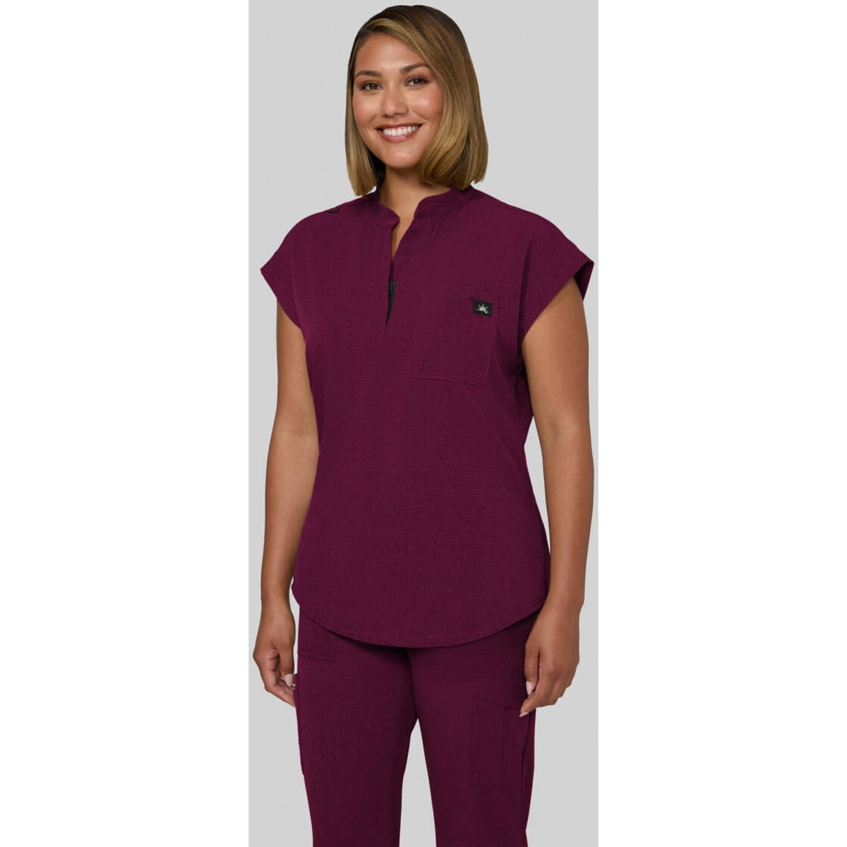 A purple scrub top with a collar and cap sleeves, featuring a logo on the chest.