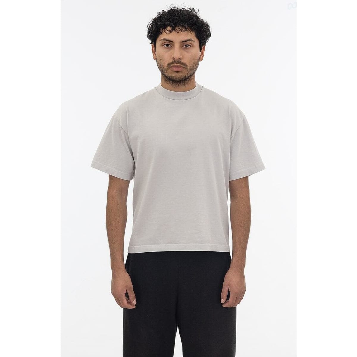A short sleeve garment dye T-shirt in light grey, displayed on a model. The shirt has a simple design and a logo.