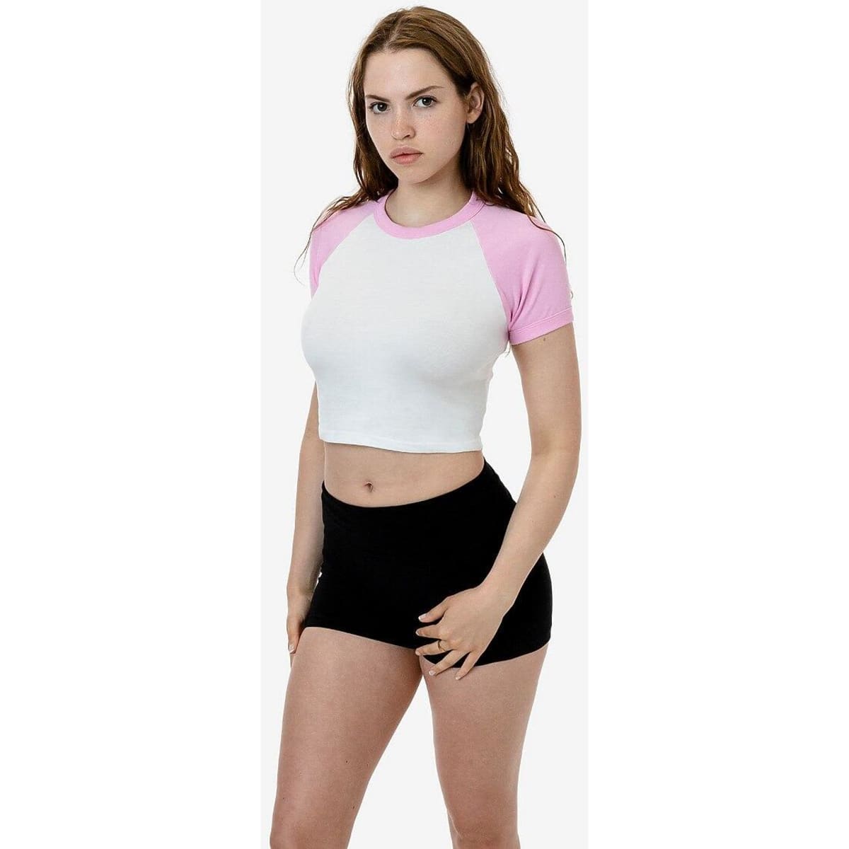 A short sleeve baby rib raglan tee with a white body and pink sleeves, displayed on a model wearing black shorts.