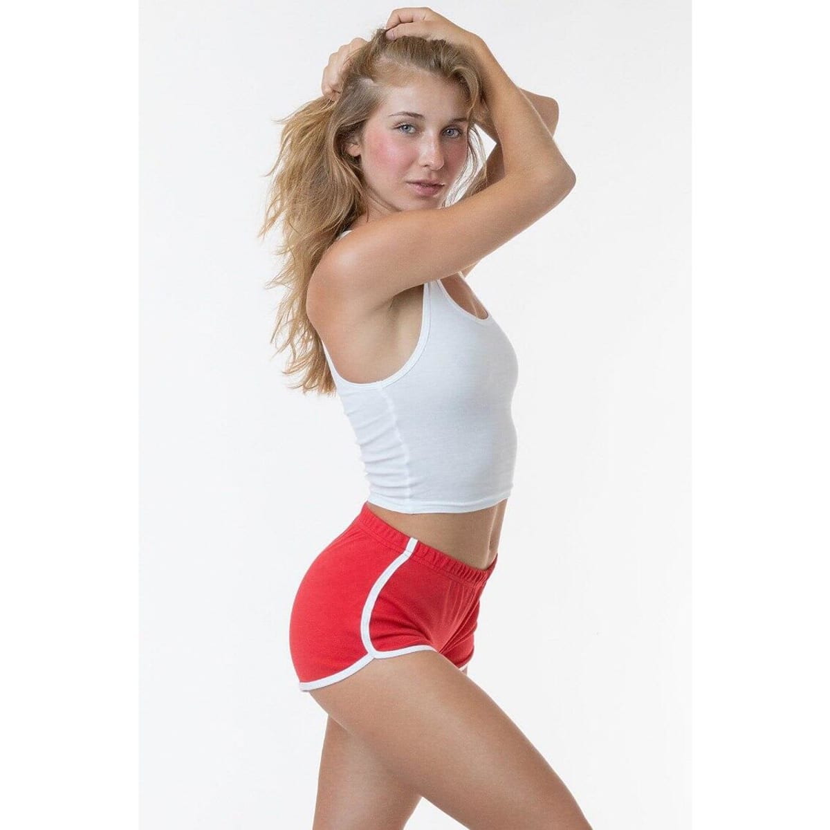 Red running shorts with white piping, displayed on a model wearing a white tank top. The image features a branding logo.