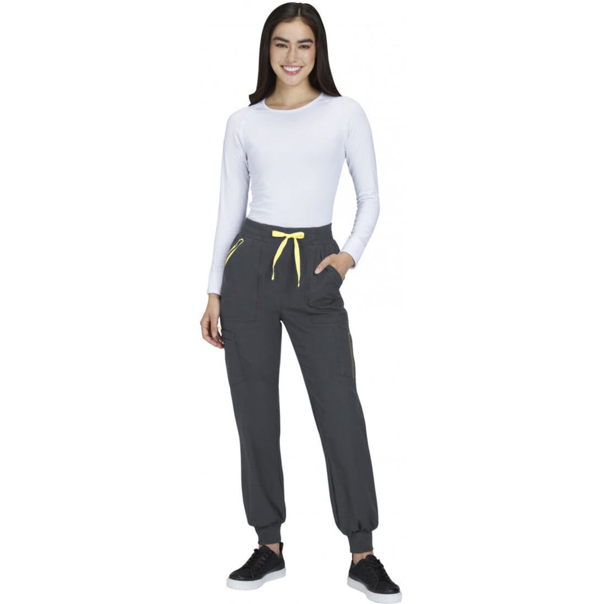 A woman wearing grey joggers with yellow drawstrings and pockets, paired with a white long-sleeve top and black shoes.