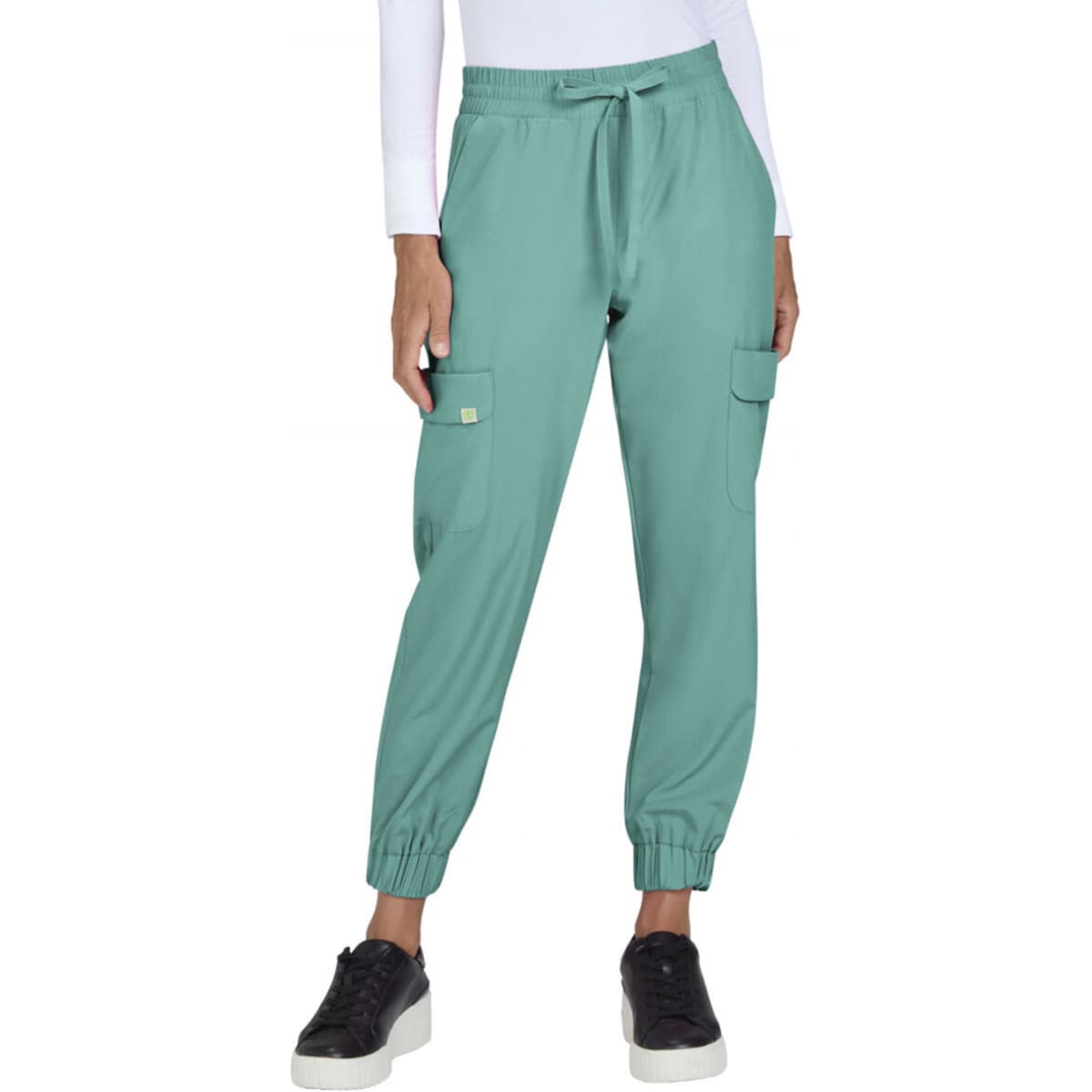 A pair of teal jogger pants featuring cargo pockets and elastic cuffs, worn with black shoes. The model is indoors.