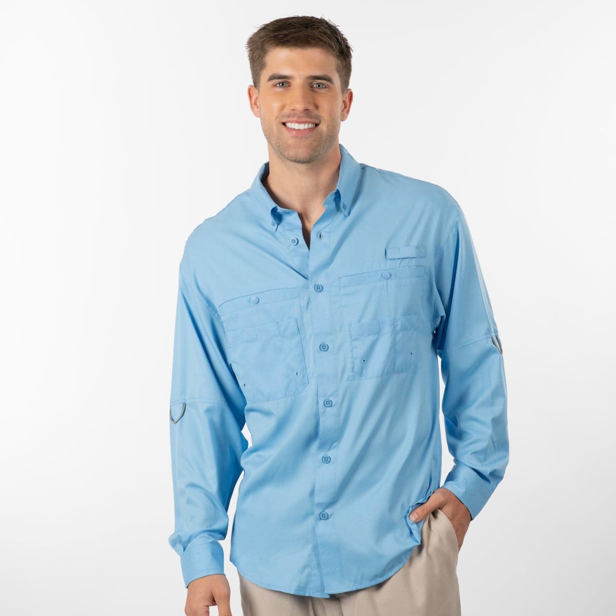 A man stands by the water wearing a light blue long-sleeve fishing shirt, holding a fishing rod and a cooler.
