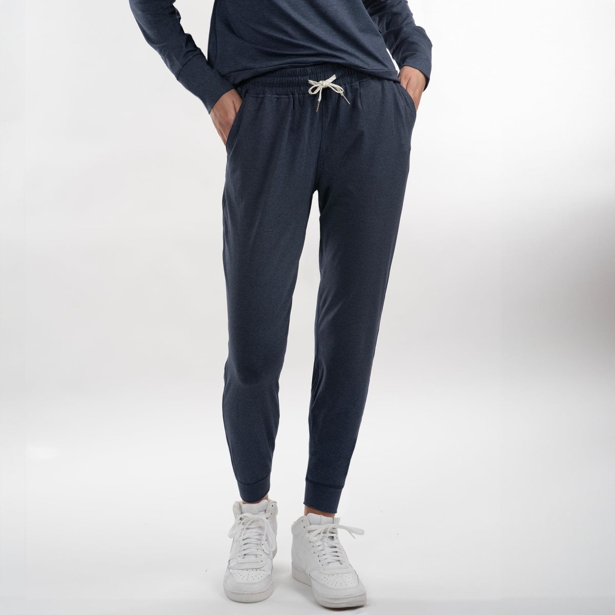 A pair of navy soft jersey joggers with an elastic waist and pockets, worn with a top and white sneakers.