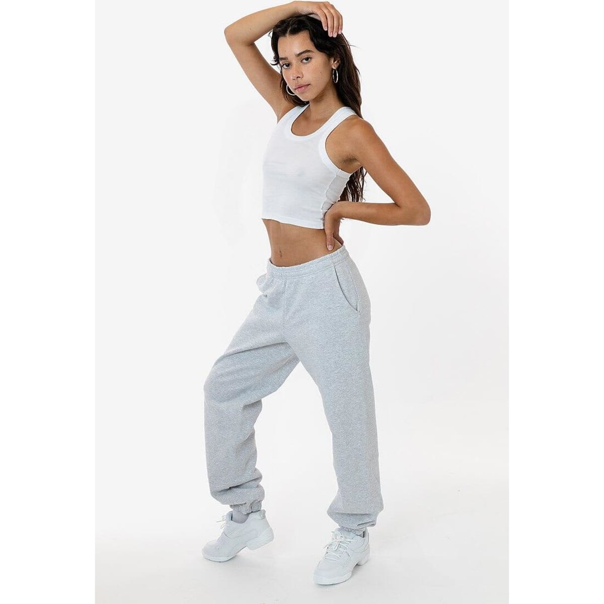 A model poses in grey heavy fleece sweatpants, paired with a cropped white tank top and white sneakers.