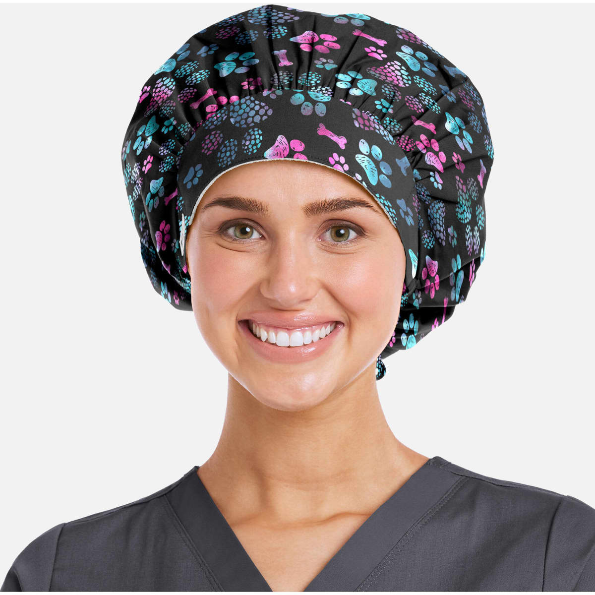 A bouffant cap featuring a black background with colourful floral and paw print patterns. The model is smiling.