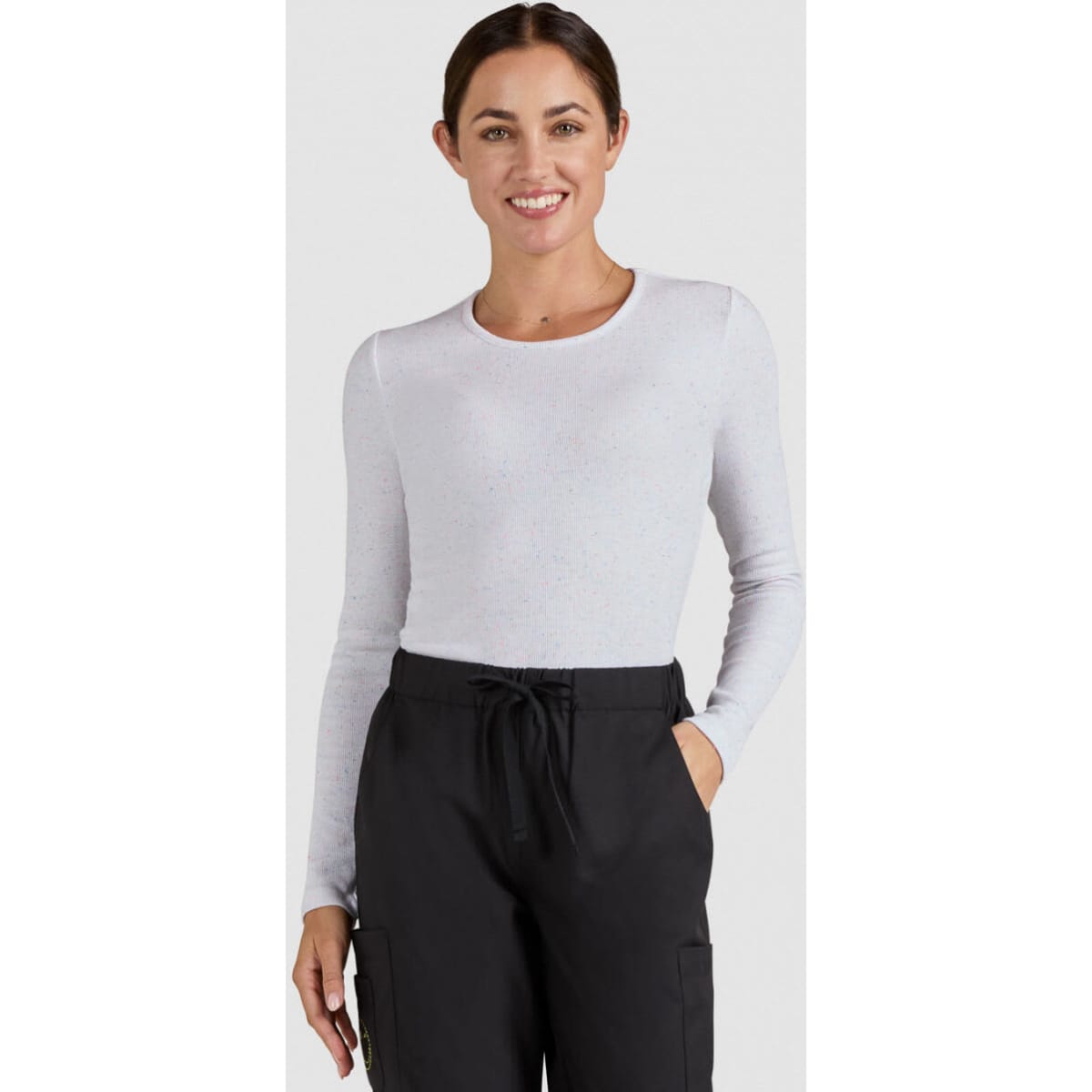 A woman wearing a long-sleeve, light grey top paired with black pants, smiling at the camera.