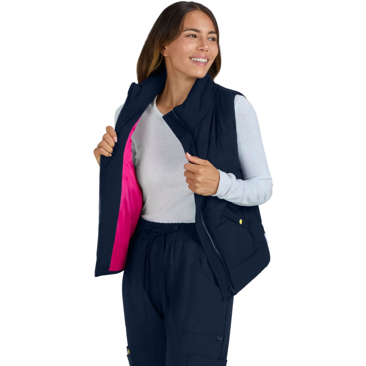 A woman wearing a navy blue vest, unzipped to reveal a bright pink interior, smiling while standing.