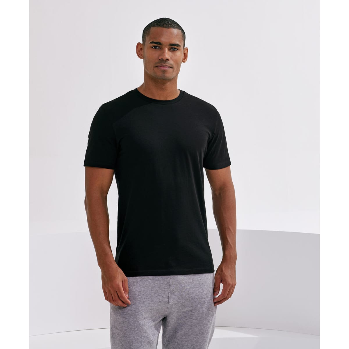 A black organic T-shirt displayed on a male model, paired with grey sweatpants. The garment features a logo.