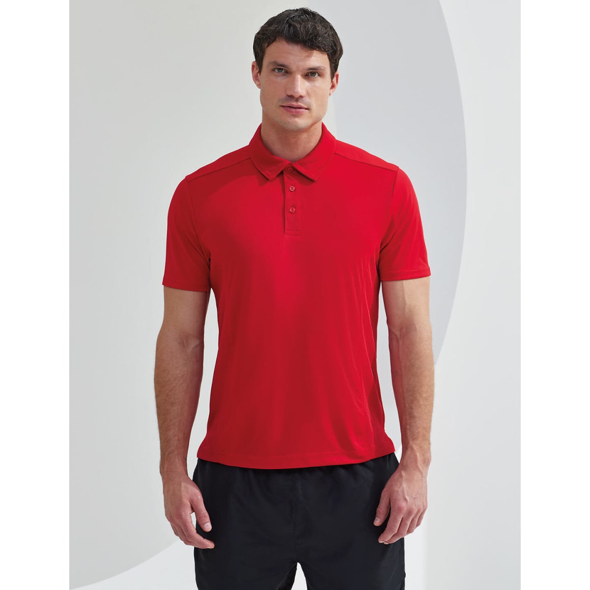 A man wearing a red panelled polo shirt stands against a light background, featuring short sleeves and a collar.