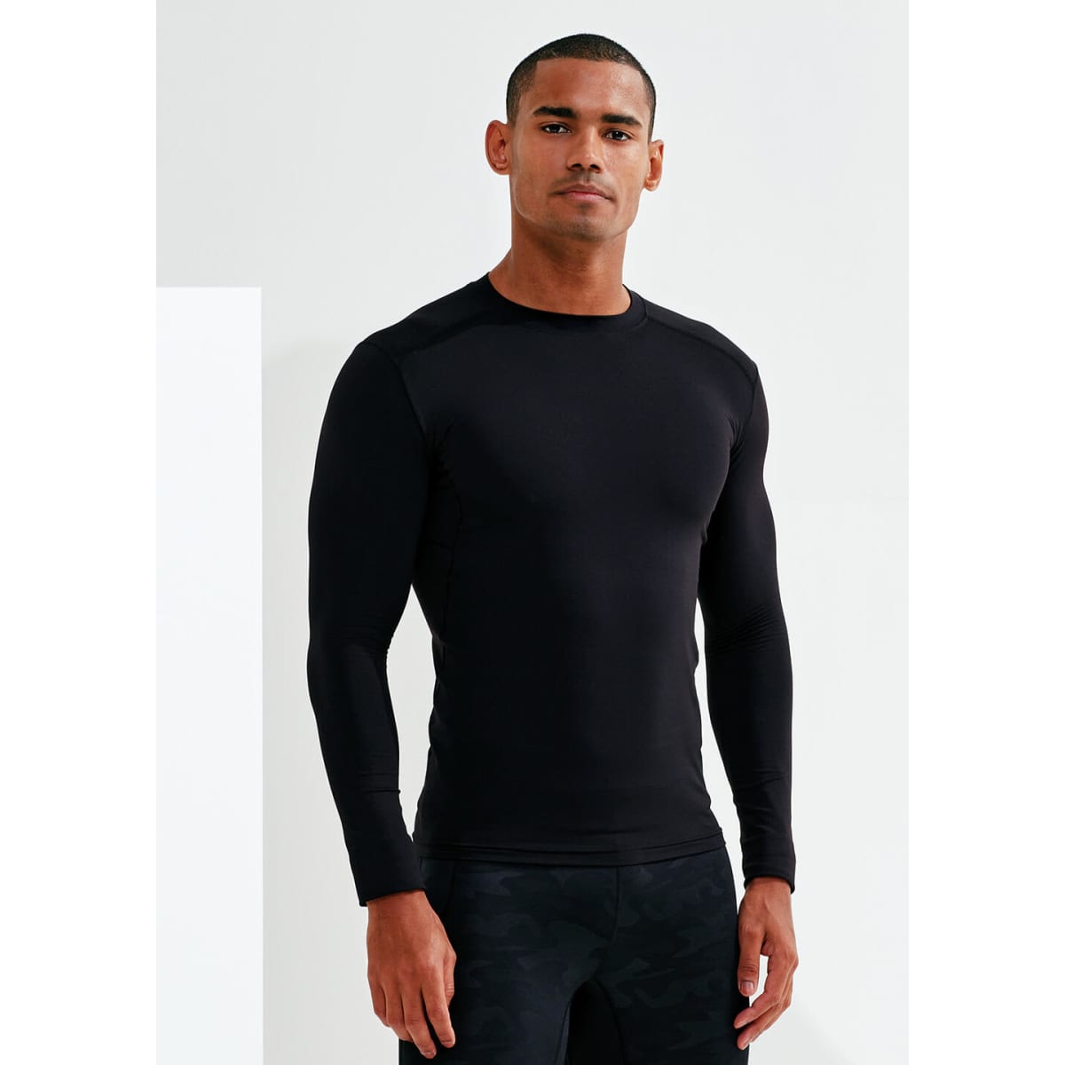 A fitted black long-sleeve top worn by a model, featuring a sleek design and a logo.