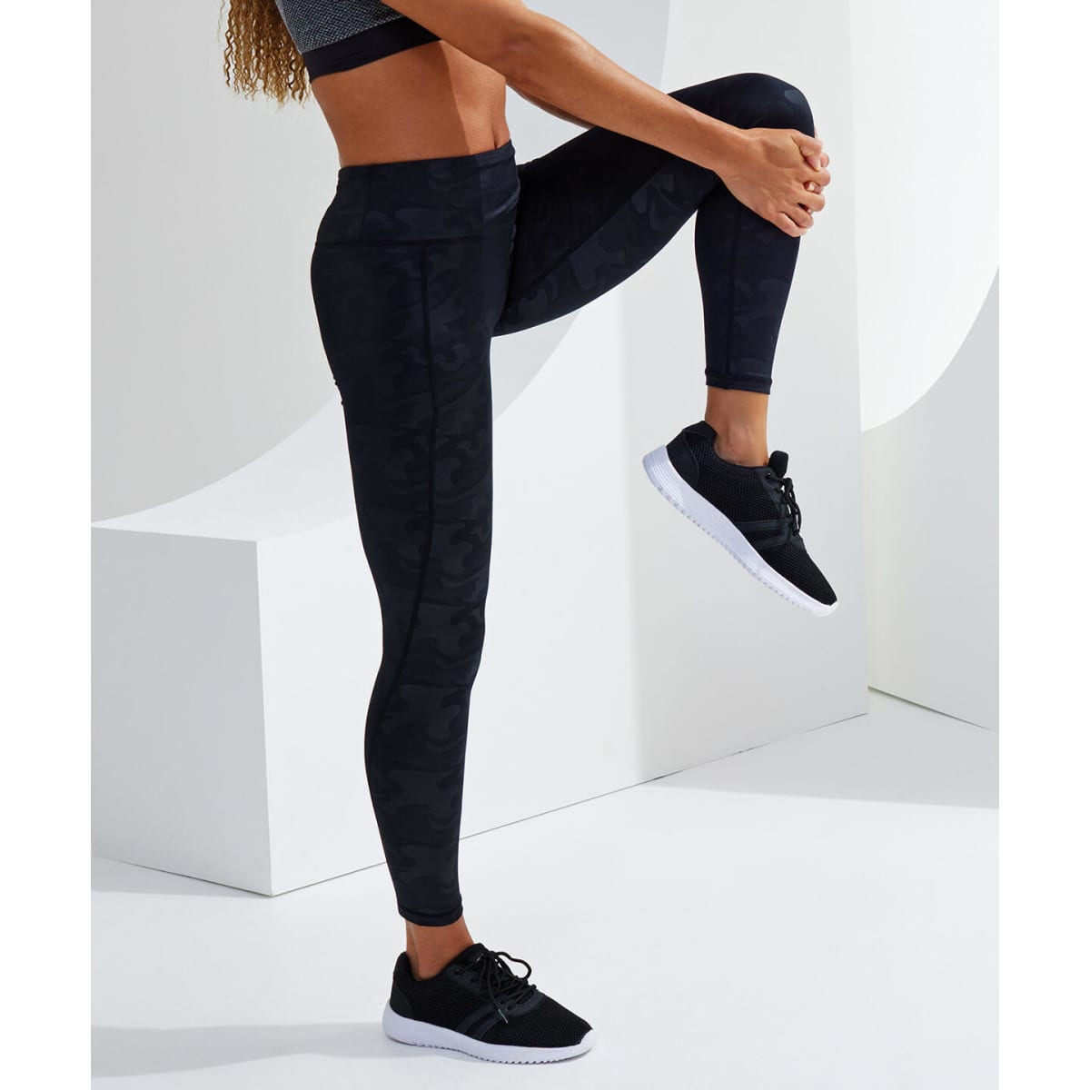 Full-length leggings in dark camo print, paired with a matching top and black athletic shoes. The model poses dynamically.