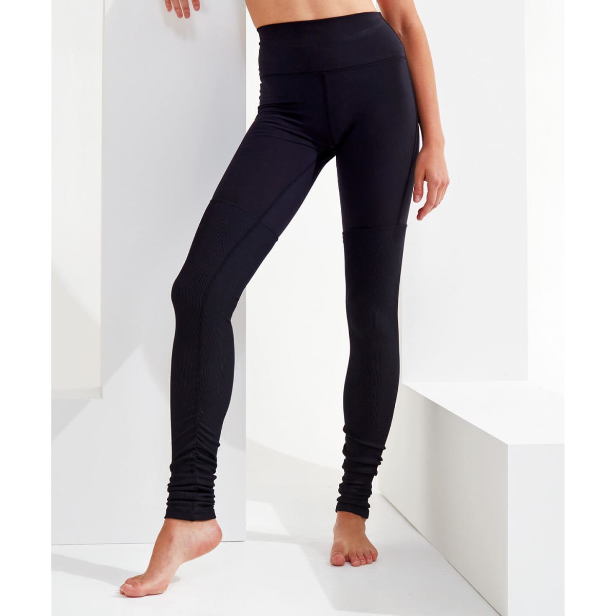 Black yoga leggings displayed on a model, featuring a high waistband and a fitted design. The setting is minimalist.
