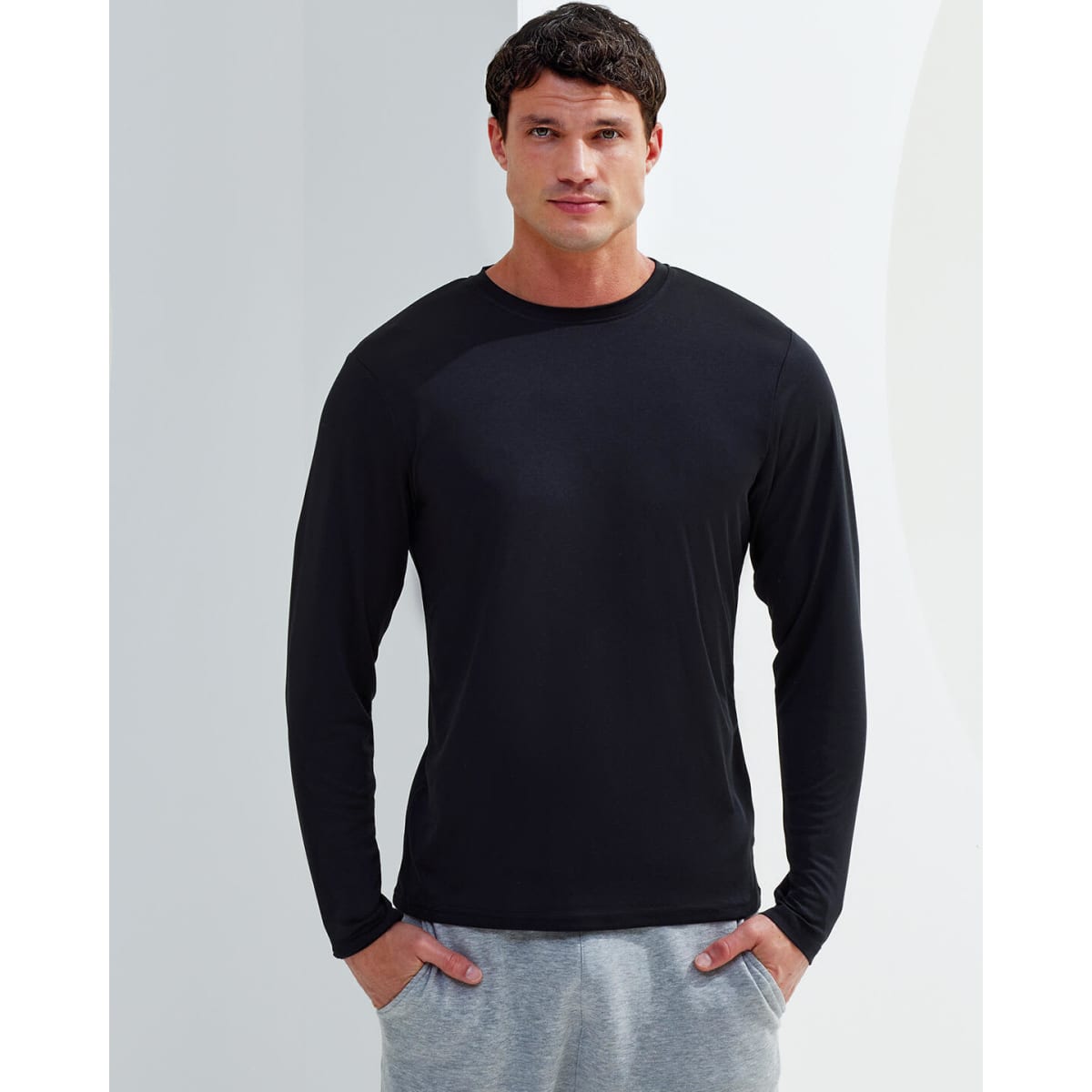 A long sleeve performance t-shirt in black, worn by a model, paired with grey pants. The shirt features a logo.