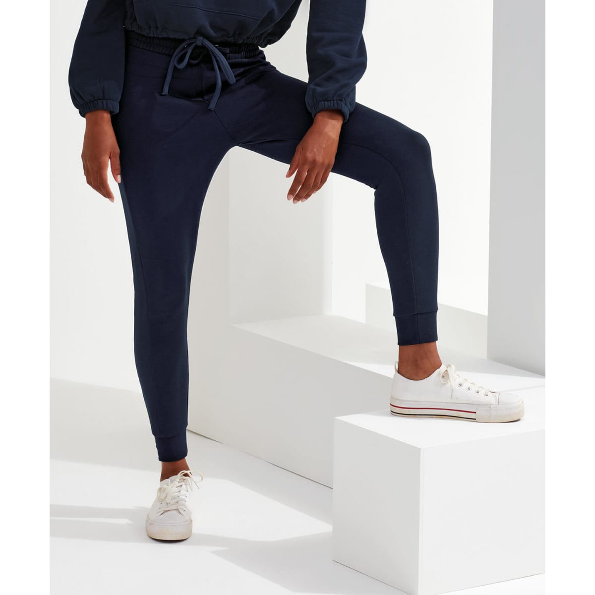 Fitted joggers in navy blue with a drawstring waist. A stylish and comfortable fit. White sneakers complement the look.