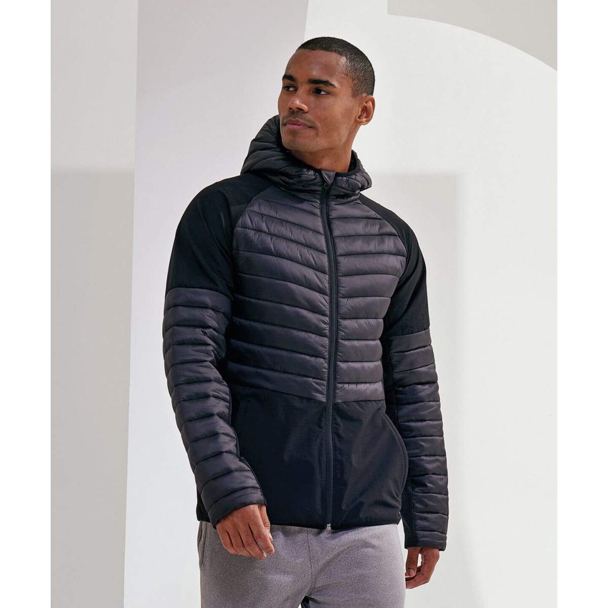An insulated hybrid jacket in black and grey, featuring a zip front and hood, worn by a model.