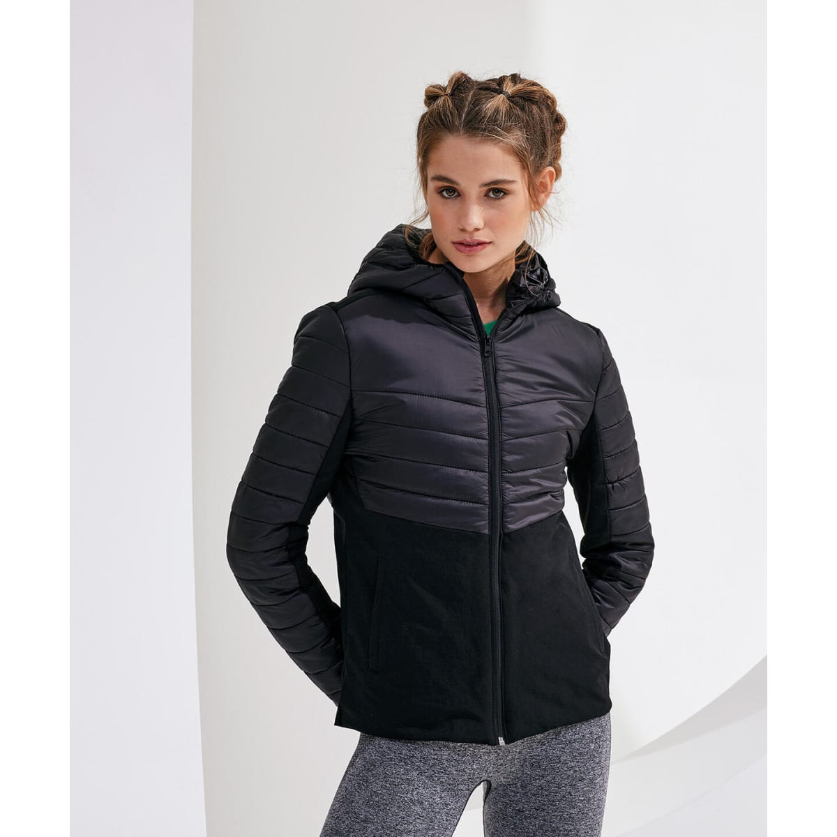 A woman wearing a black insulated hybrid jacket with a hood, featuring quilted panels and a sleek design.