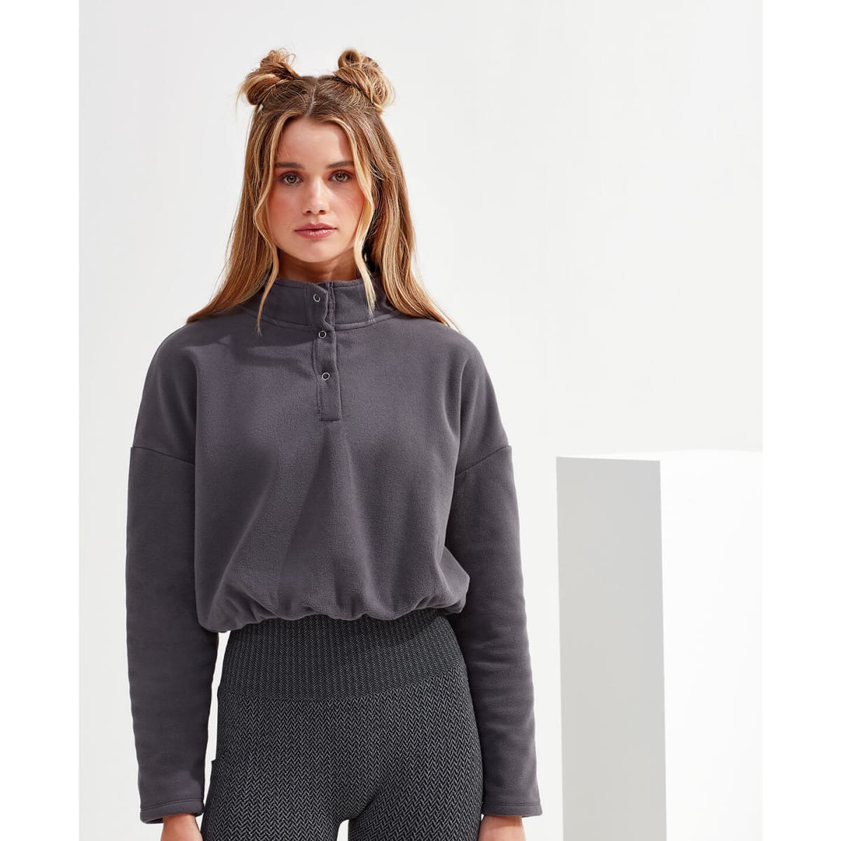 A grey cropped fleece top with a high collar and button detailing, paired with textured, high-waisted leggings.