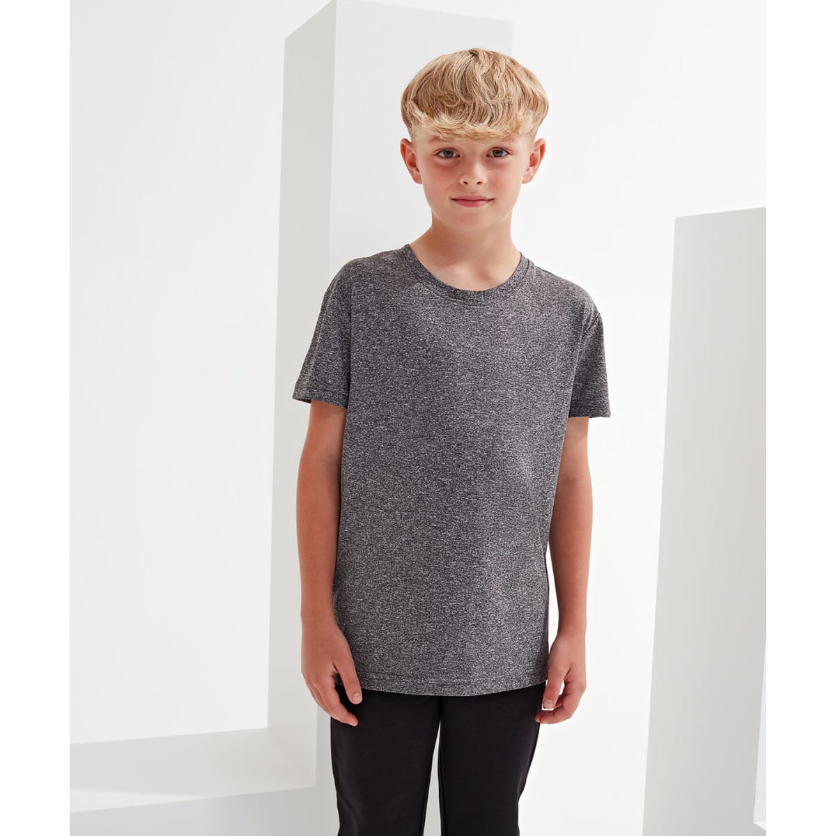 A grey kids' performance t-shirt displayed on a boy against a minimalist background. The shirt has a simple design.