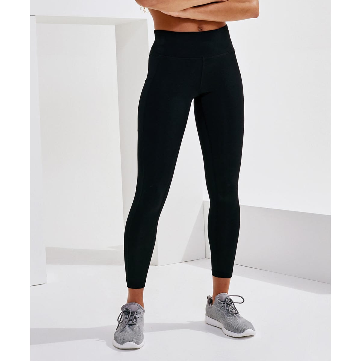 Performance leggings in black with pockets, paired with grey athletic shoes, displayed against a minimalist white background.
