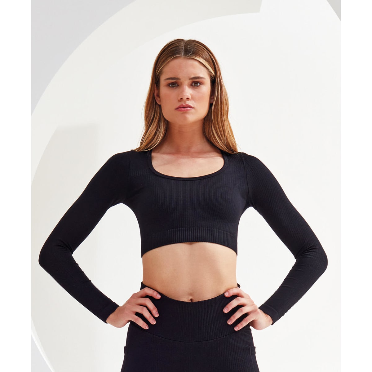 A ribbed, seamless black crop top with long sleeves and a scoop neckline. It features a fitted design and has a logo.