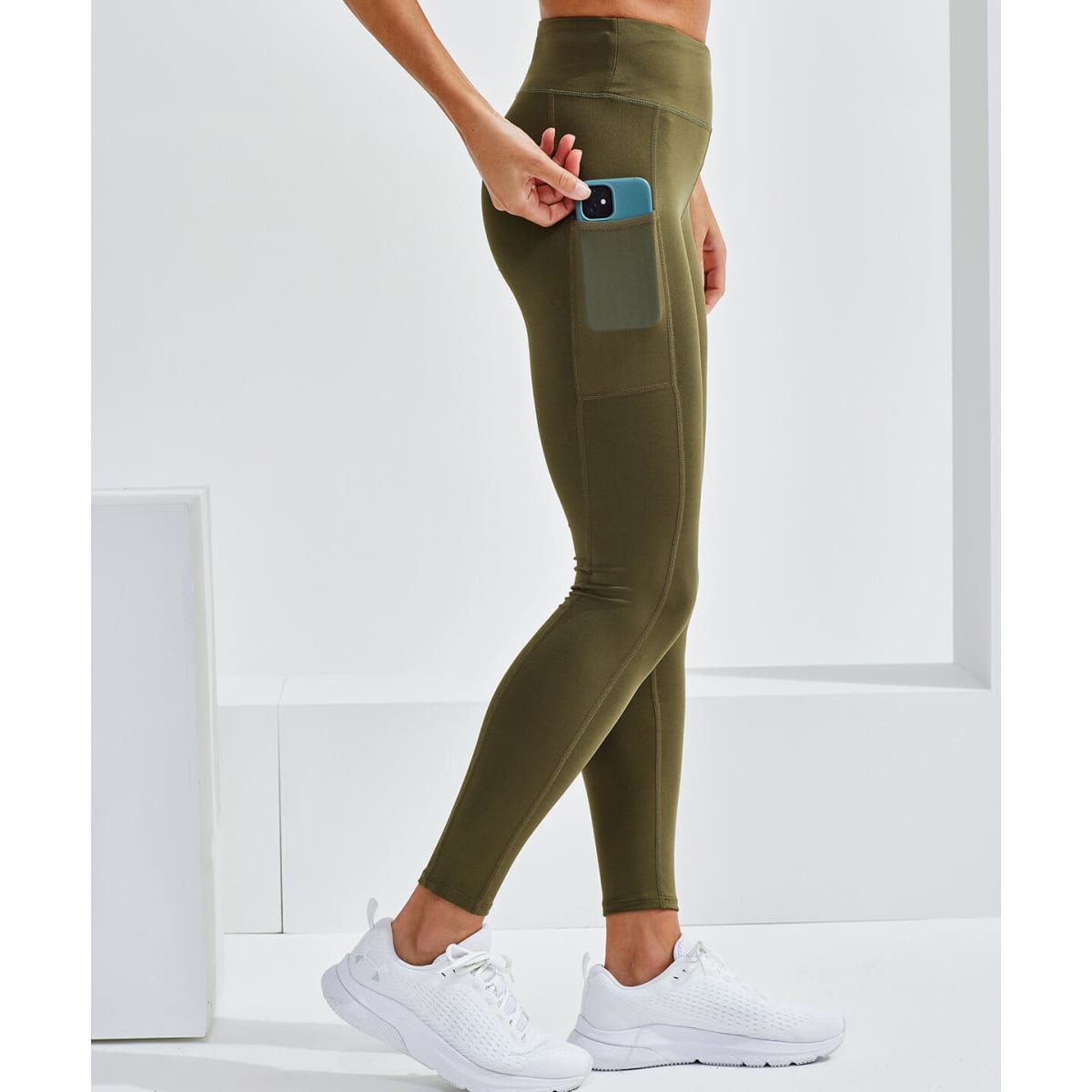 Performance compression leggings in olive green with a side pocket and a person wearing white sneakers. Includes a logo.