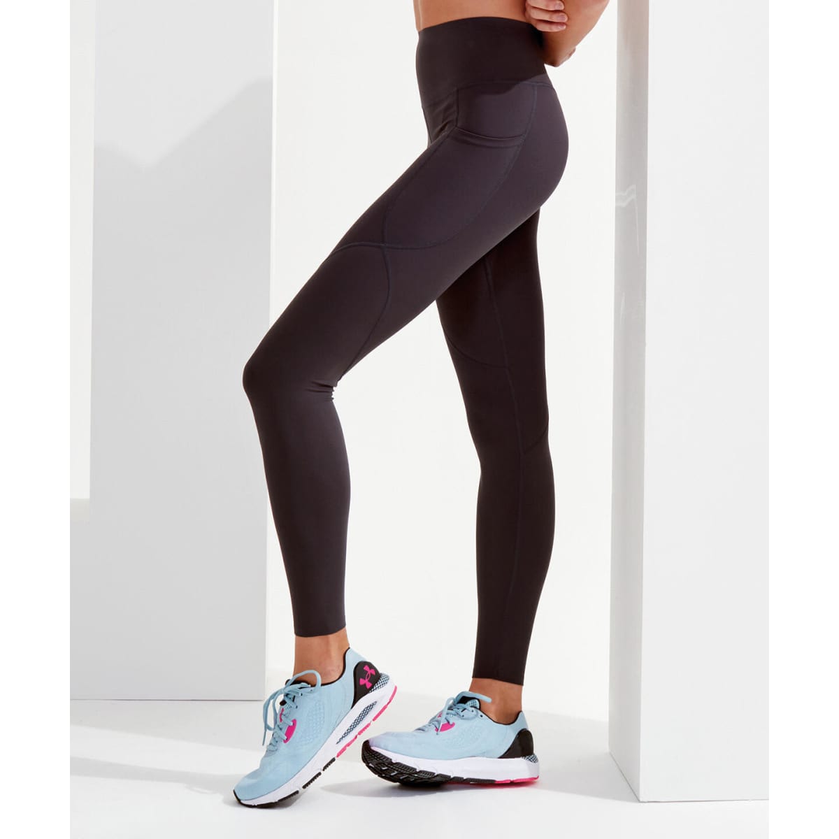 Black leggings with a high waist, paired with light blue and pink athletic shoes against a minimalist background.