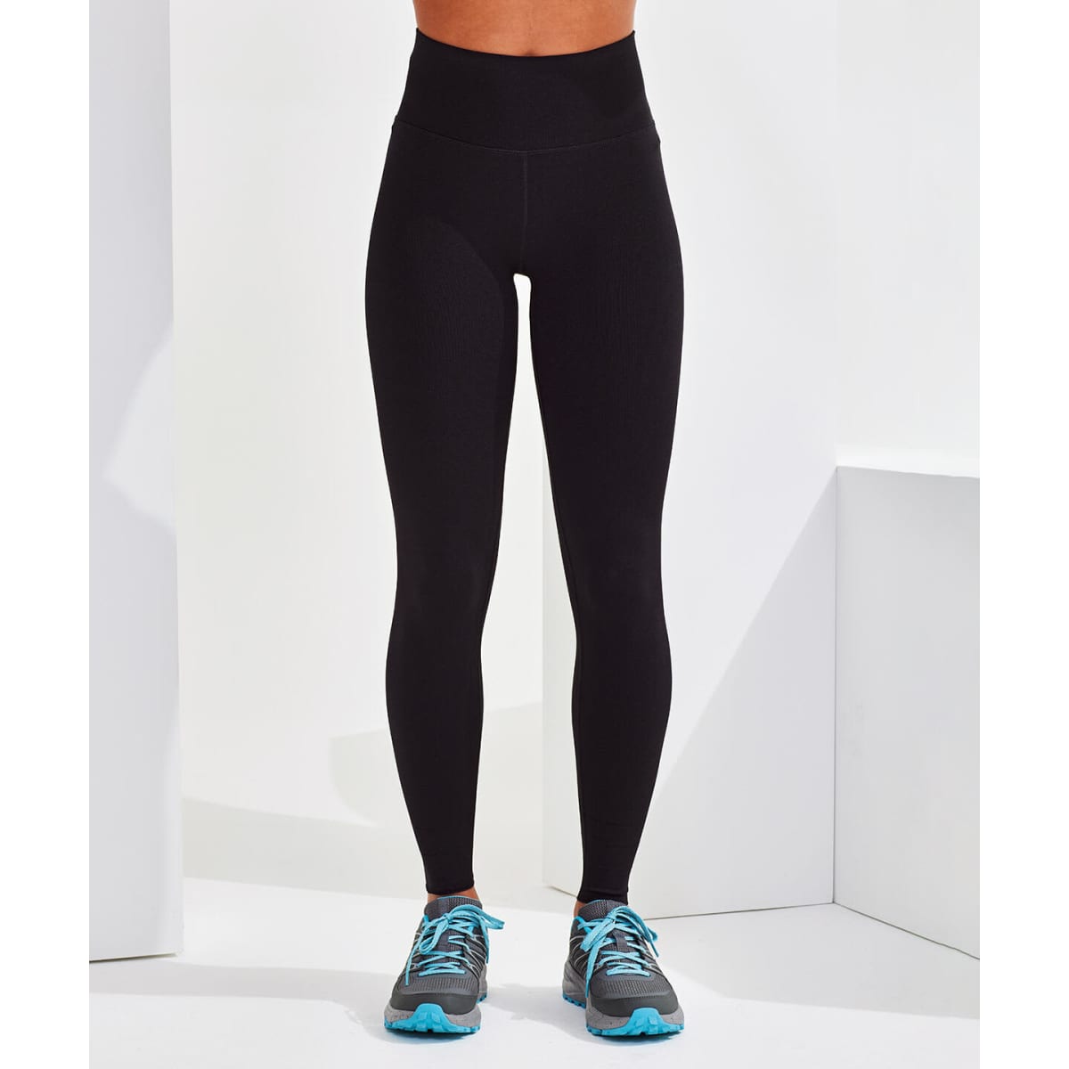 A pair of black seamless leggings displayed on a model, paired with grey and blue athletic shoes.
