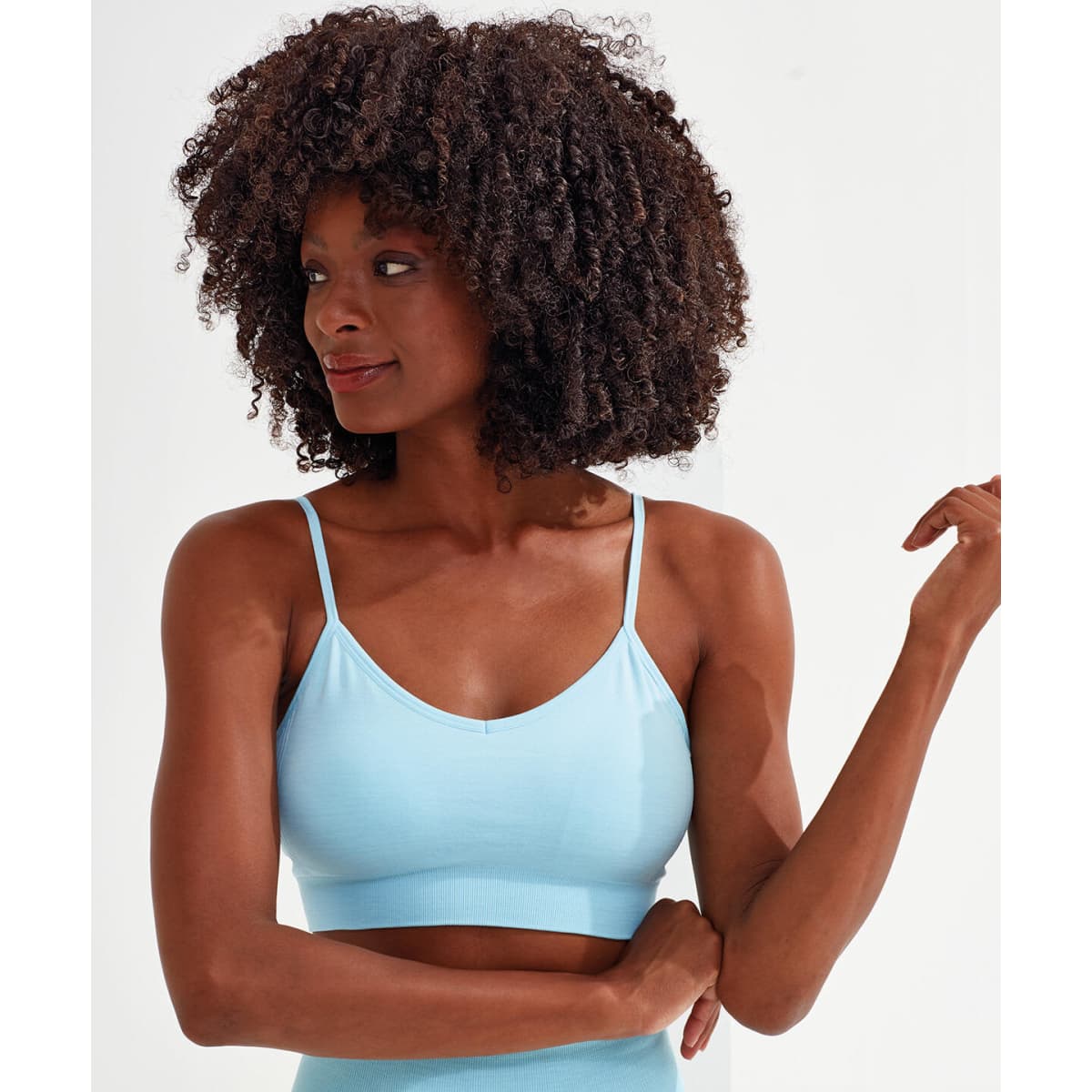 A light blue sport bra with seamless design and thin straps, featured on a model with curly hair and a neutral background.