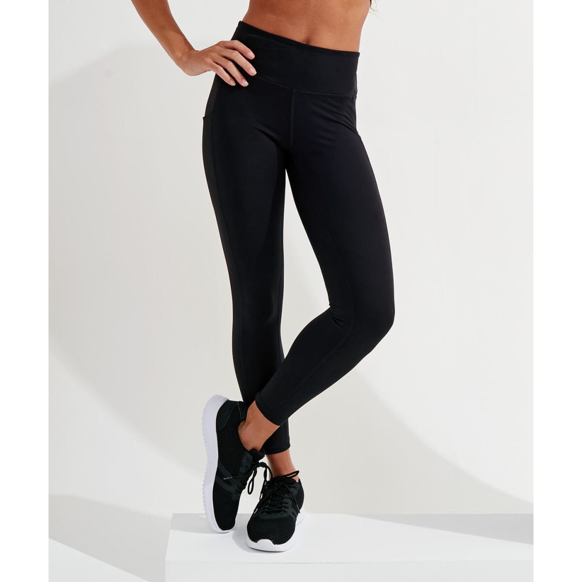 Black full-length leggings made from recycled materials, displayed on a model wearing black sneakers.