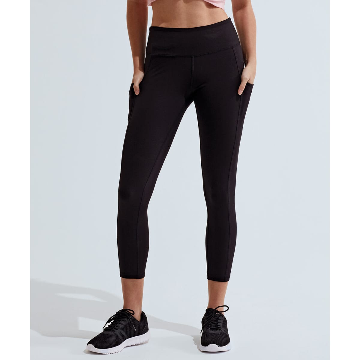 Black 7/8 leggings with a fitted design and side pockets. Model is wearing black athletic shoes.