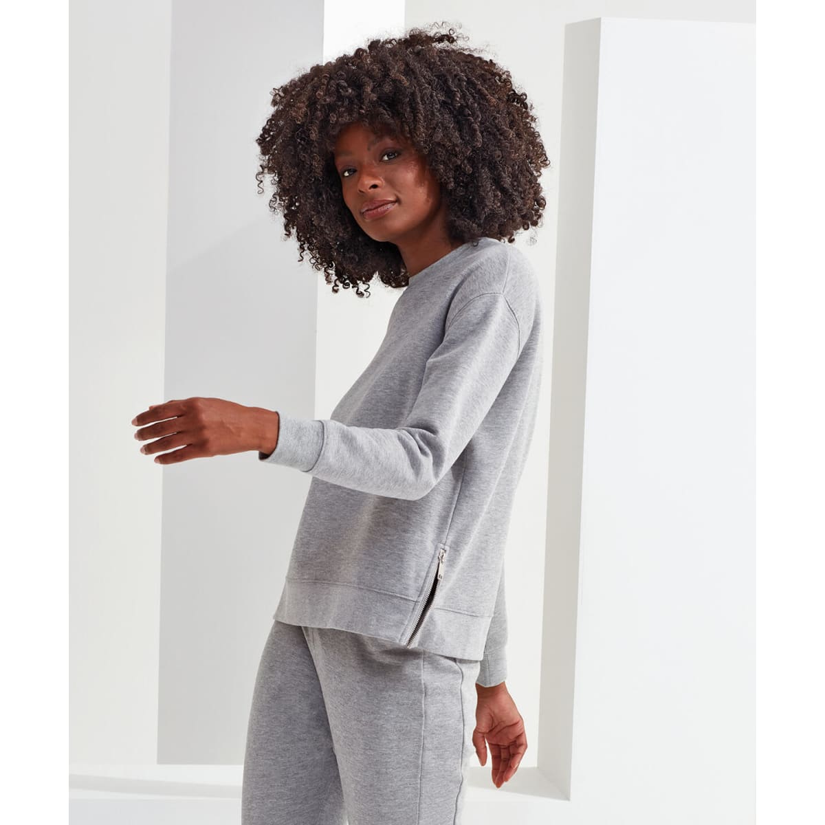 A grey sweatshirt featuring a zip detail, shown on a model with curly hair, against a minimalist background.