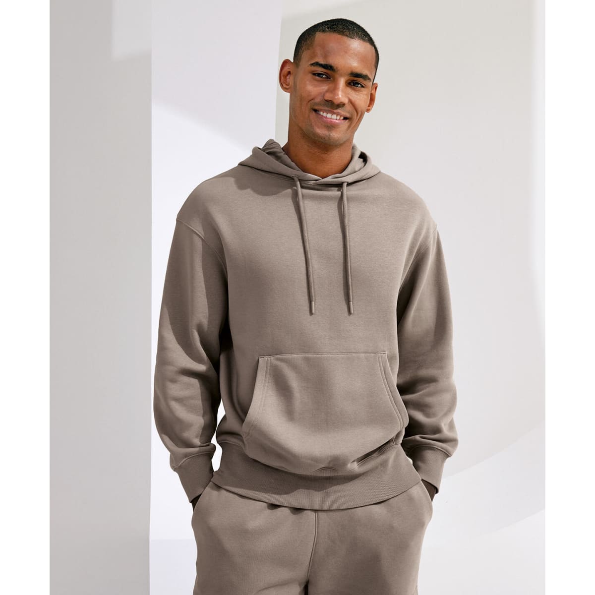 A unisex recycled hoodie in a neutral brown shade features a front pocket and an adjustable drawstring hood.