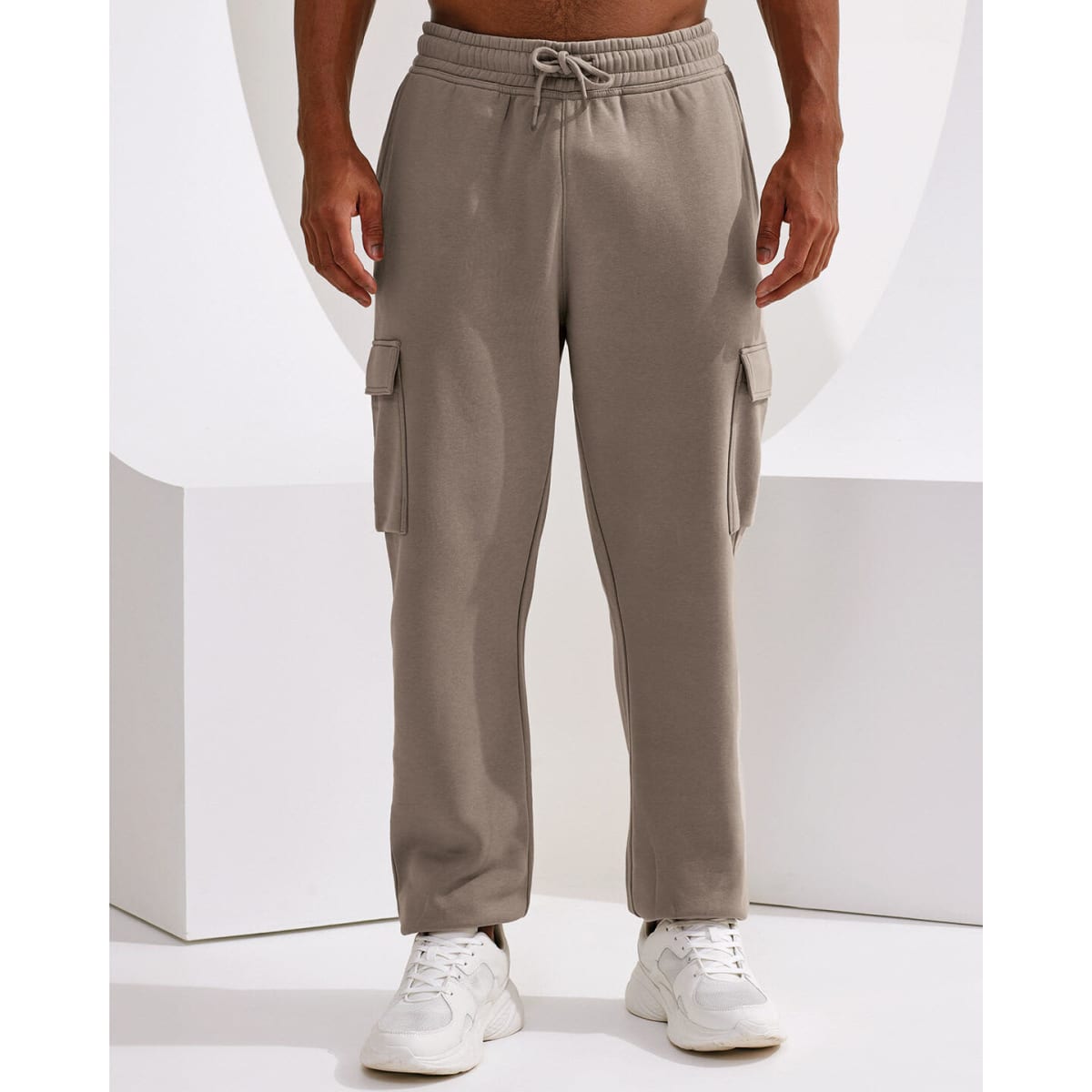 Unisex cargo joggers in a light beige colour with side pockets and a drawstring waist, featuring a logo.