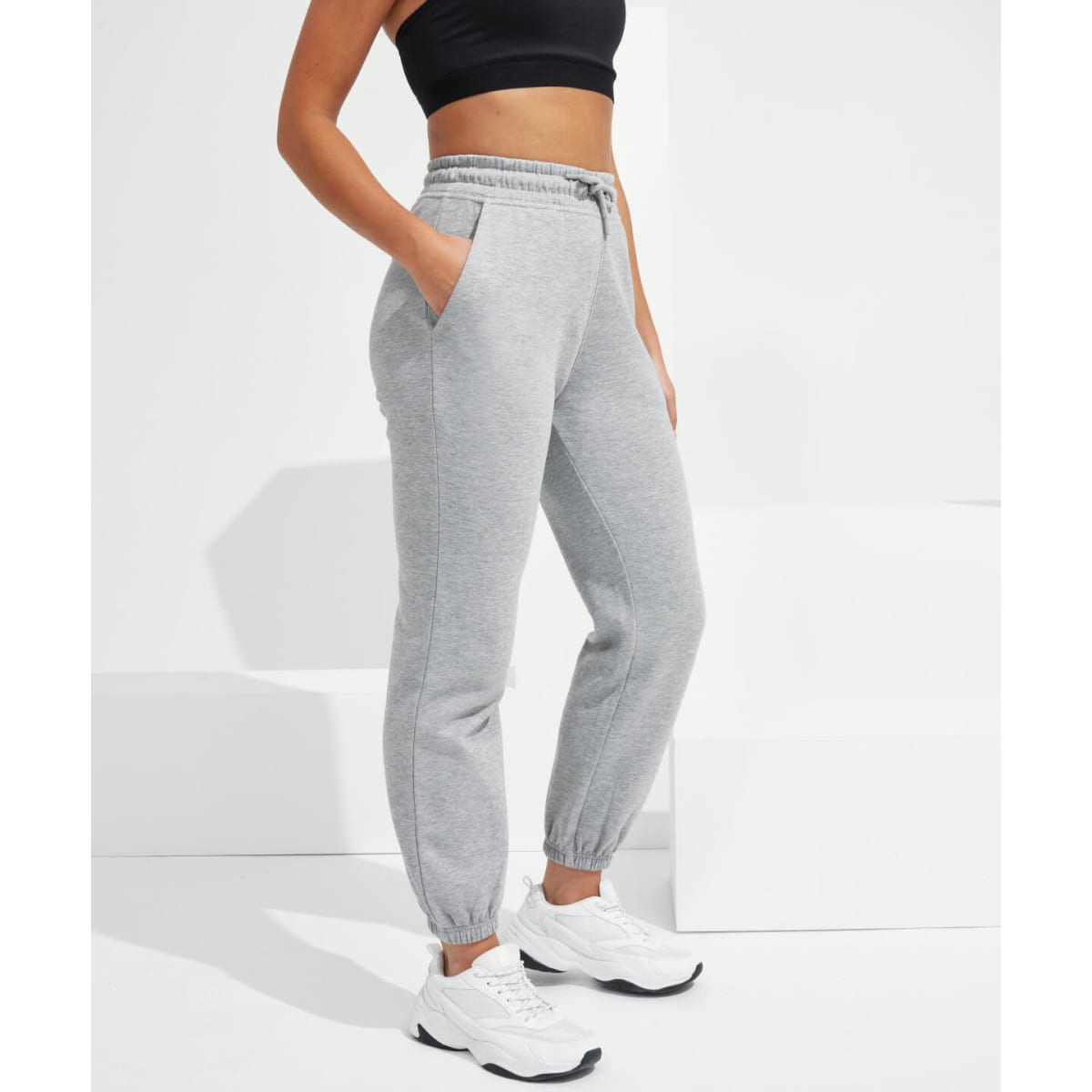 A pair of grey unisex joggers with an elastic waistband and pockets, displayed on a model.