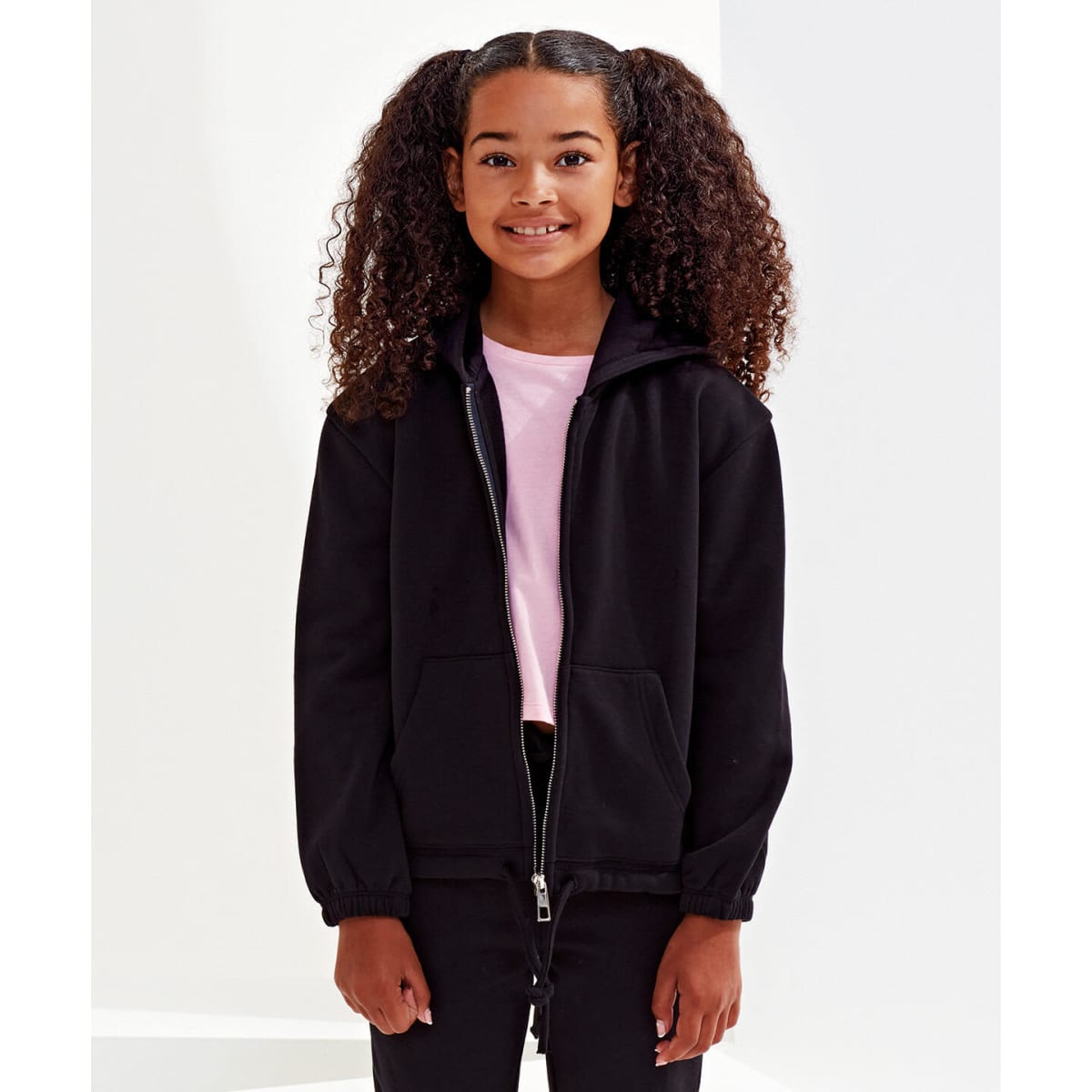 A girl wearing a black cropped oversized full-zip hoodie with curly hair. The hoodie features a hood and zip fastening.