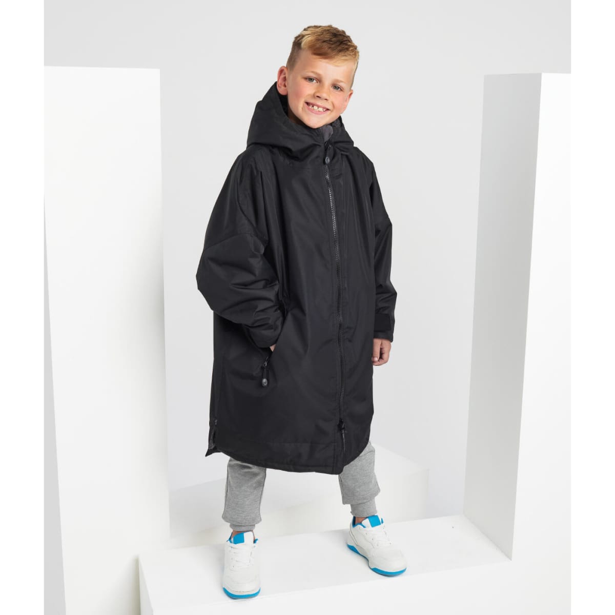A black waterproof changing robe with a hood, worn by a child standing on a white display.